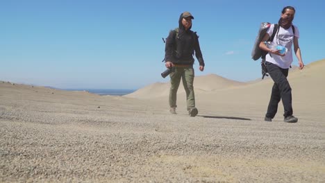 Toma-De-Tierra-De-Dos-Campistas-Caminando-En-El-Salvaje-Desierto-De-Paracas-Bajo-El-Sol,-California