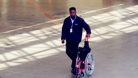 African-American-airport-worker-transporting-folded-wheelchair,-super-slow-motion