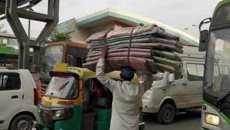 Indischer-Mann-Trägt-Ein-Großes-Bündel-Auf-Dem-Kopf-Und-Wartet-Darauf,-Die-Straße-Zu-überqueren,-Delhi,-Indien