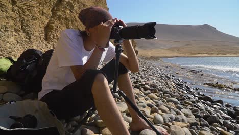Person-Looking-Through-Professional-Camera-Lenses-To-Sea-Horizon-On-Pebble-Beach