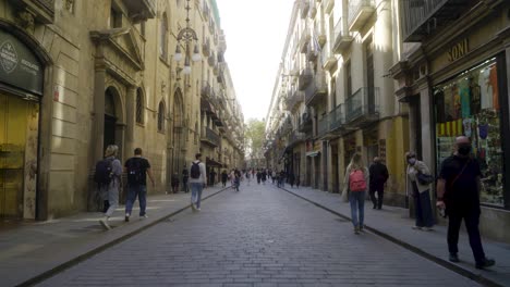 Forward-shot-through-long-central-street-in-Barri-Gothic-quarter-of-Barcelona-with-people-starting-their-day-in-the-morning-and-walking-over-pavement