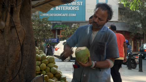 Tender-coconut-seller-peeling-coconut-shell-using-sharp-knife-at-street