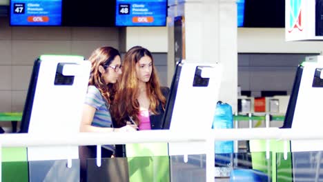 Mother-and-daughter-checking-in-at-a-self-service-kiosk-in-the-airport,-slow-motion