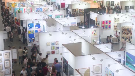 Bird's-eye-view-of-visitors-attending-an-art-fair-show-where-art-exhibitors-sell-paintings-and-sculptures-to-visitors,-art-enthusiasts,-and-collectors