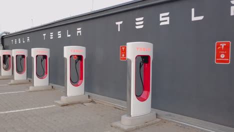 Tesla-Electric-Car-Supercharger-Charging-Stations,-without-people,-near-a-grey-wall-in-the-parking-lot-on-the-terrace-of-a-mall-in-Romania---close-pan-left-day-view
