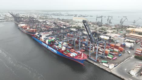 Aerial-View-Of-Cargo-Container-Ship-Docked-At-Terminal-Beside-Gantry-Cranes-At-Karachi-Port-Trust-Terminal