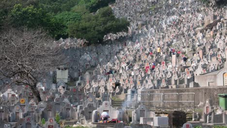 During-the-Chung-Yeung-Festival,-a-woman-burns-offerings-in-front-of-her-deceased-relatives'-graves-at-a-crowded-cemetery