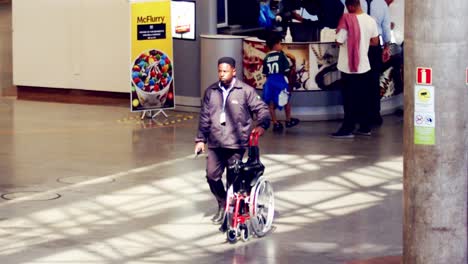 Black-African-American-worker-rolling-folded-wheelchair-in-airport,-slow-motion