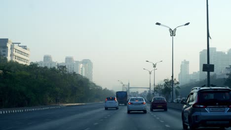 Driving-a-car-on-the-Mumbai-highway-towards-Panvel,-Lonavala,-Pune,-Goa-before-sunrise-with-Mumbai-skyline-buildings-in-view
