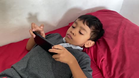 Ein-4-jähriger-Asiatischer-Junge-Spielt-Auf-Seinem-Smartphone,-Während-Er-Im-Bett-Liegt