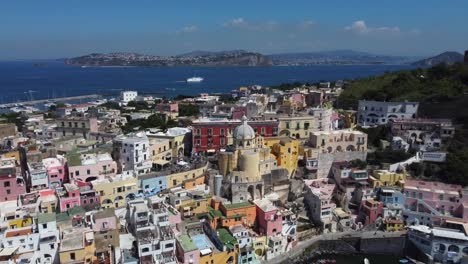 -Procida-island-with-Marina-di-Corricella-visible,-low-rise-traditional-colorful-houses-and-moored-boats-in-Campania-Region,-Italy