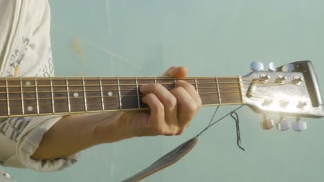 Close-up-of-hand-of-young-man-playing-the-guitar-during-sunset-by-the-water-at-the-commercial-harbour-of-Barcelona,-Spain