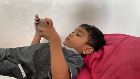 Ein-4-jähriger-Asiatischer-Junge-Spielt-Auf-Seinem-Smartphone,-Während-Er-Im-Bett-Liegt
