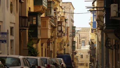Cars-Parking-In-A-Narrow-Street-Under-The-Traditional-Colourful-Balconies-In-Valletta