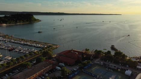 Drone-aerial-forward-fast-moving-flying-view-of-Portoroz-with-boats-in-sea-in-yellow-sunset-light,-Slovenia