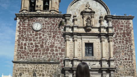 Parroquia-Santiago-Apostol-landmark-tilt-down-revealing-brunette-model-walking-in-Tequila-town-square-in-Jalisco,-Mexico---Slow-motion