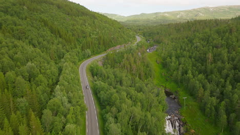 Camper-van-driving-on-scenic-road-next-to-river-and-lush-green-forest-in-Norway