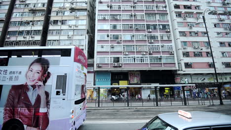 Menschen-Und-Fahrzeuge-Auf-Der-Belebten-Straße-Vor-Geschäfts--Und-Wohngebäuden-In-Hongkong---Zeitraffer