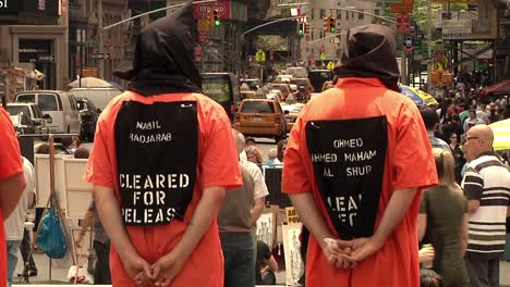 Locked-Off-View-Of-Adult-Males-Wearing-Black-Hoods-In-Orange-Prison-Jumpsuit-Protesting-In-NYC