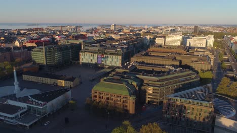 Aerial-view-away-from-the-Kamppi-shopping-mall,-on-a-sunny,-summer-morning-sunrise,-in-Helsinki,-Finland---pull-back,-drone-shot