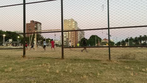 Group-of-children-playing-football-on-a-dirt-pitch,-back-view