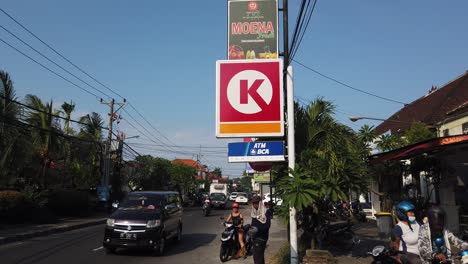 Circle-K-Logo-Shop-Entrance-in-Denpasar-Sanur-Street,-Bali-Indonesia,-Traffic-of-Cars,-Motorbikes-and-Parking-Slots,-Mini-Market-Convenience-Store
