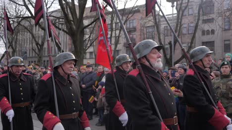 Slow-motion-track-of-disabled-veterans-marching-down-the-streets-of-Kaunas-in-military-dress-for-a-celebration-in-Lithuania,-carrying-flag-poles