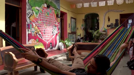 Rustic-room-with-painted-art-walls-and-a-young-male-swinging-on-hammock,-Dolly-right-shot