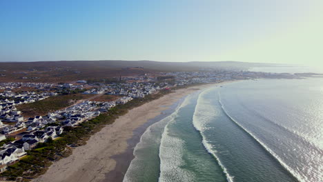 Waves-roll-onto-long-beach-lined-with-whitewashed-houses,-Paternoster