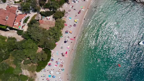 Aerial-Crane-Lowering-over-People-Sunbathing-on-Dubovica-Beach,-Hvar-Island,-Croatia