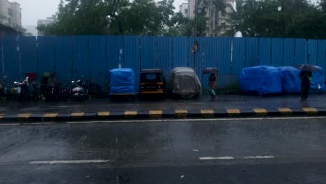Escena-De-Un-Día-Lluvioso-En-La-Calle-En-Mumbai,-India,-Con-Vehículos-Tuk-tuk-Cubiertos-Estacionados-Al-Fondo---Toma-Amplia