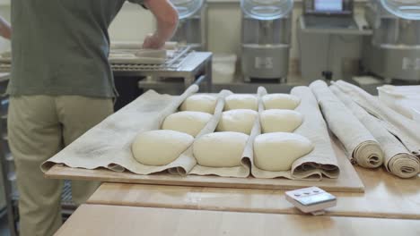 Rows-Of-Fresh-Dough-On-Fabric-Placed-On-Table-With-Worker-In-The-Background