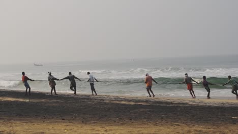 Locals-of-a-traditional-fishing-village-in-Kappil-Beach,-Varkala,-India-hauling-their-catch-for-the-day---wide-pan