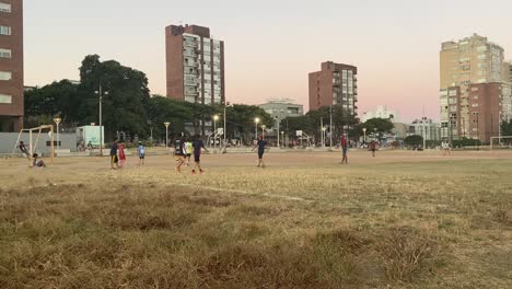 Group-of-children-playing-football-on-a-dirt-pitch,-pan