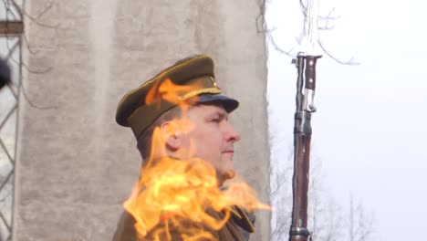 Looking-through-the-flickering-fire-of-the-eternal-flame-to-see-a-soldier-standing-guard-next-to-the-torch-in-Kaunas,-Lithuania-for-the-restoration-of-the-state-celebration