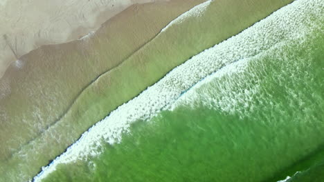 Diagonal-top-drone-view-as-waves-run-out-onto-sandy-beach-from-aquamarine-ocean