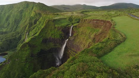Big-waterfall-lot-of-power-in-middle-of-lush-green-vegetation-in-Azores,-aerial