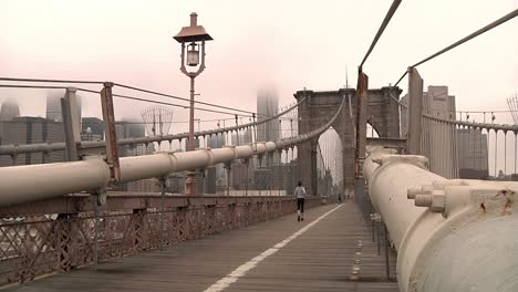 Female-Running-Past-On-A-Misty-Morning-On-Brooklyn-Bridge-In-New-York