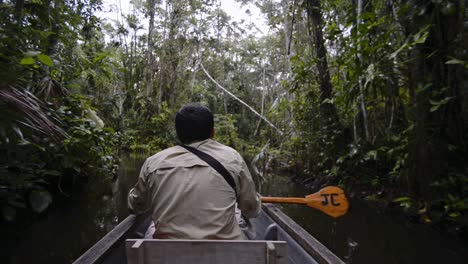 Local-man-paddling-on-a-typical-canoe-on-a-river-flowing-through-the-Amazon-rainforest,-Ecuador