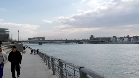 Gente-Caminando-Por-El-Paseo-Marítimo-Junto-Al-Río-Rin-En-Colonia