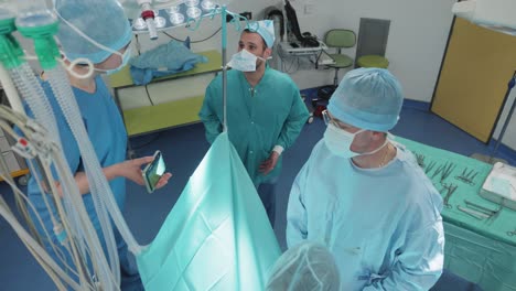 Chirurgen-Im-Operationssaal,-Assistent-Hält-Das-Telefon-Des-Chirurgen,-Sauerstoffschläuche,-Medizinische-Instrumente-Und-Die-Sterile-Umgebung-Im-Blick