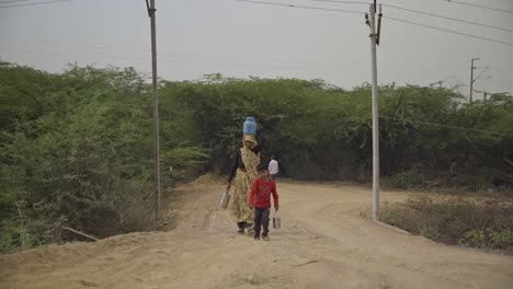 Indigenous-women-farmer-and-son-carrying-water-and-food-in-tiffin-boxes-for-lunch,-India