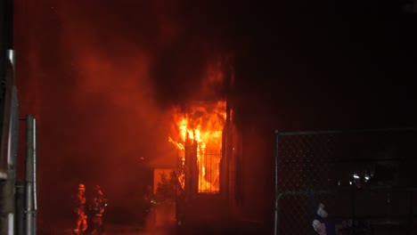 Firefighters-extinguishing-a-house-in-flames,-structure-fire,-nighttime-in-LA,-USA