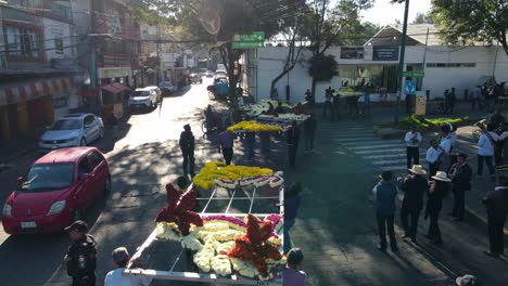 Bird's-eye-view-of-dolly-in-tracking-of-Iztapalapa-carnival-group-of-people-carrying-giant-flower-arrangements,-CDMX,-Mexico