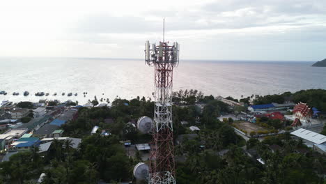 Aerial-view-of-Koh-Tao-ferry-terminal-and-town,-Sairee-Beach-view-at-sunset,-Telecommunication-mobile-tower-at-beach-island