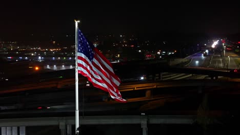 Nationalflagge-Von-Amerika-Weht-Im-Wind-Mit-Der-Autobahn-Im-Hintergrund-In-Der-Nacht