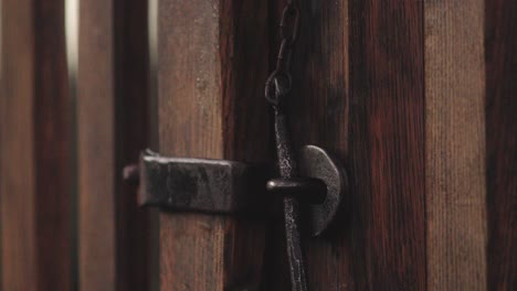 Close-up-of-a-hand-closing-an-old-wooden-gate-with-a-metal-latch-on-a-chain