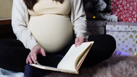 Pregnant-woman-sit-in-yoga-pose-and-flip-through-notebook-pages-near-gift-boxes