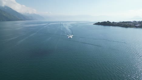 Drone-view-in-Guatemala-flying-over-a-boat-on-a-blue-lake-with-green-mountains-on-the-side-on-a-sunny-day-in-Atitlan
