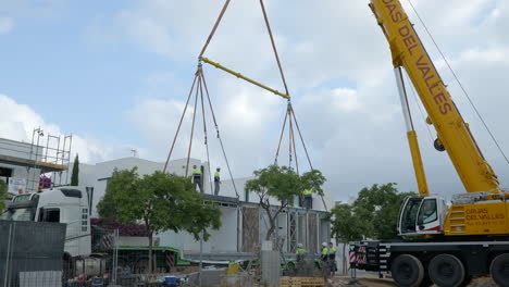 Construction-workers-lifting-smart-housing-module-by-crane-from-back-of-truck